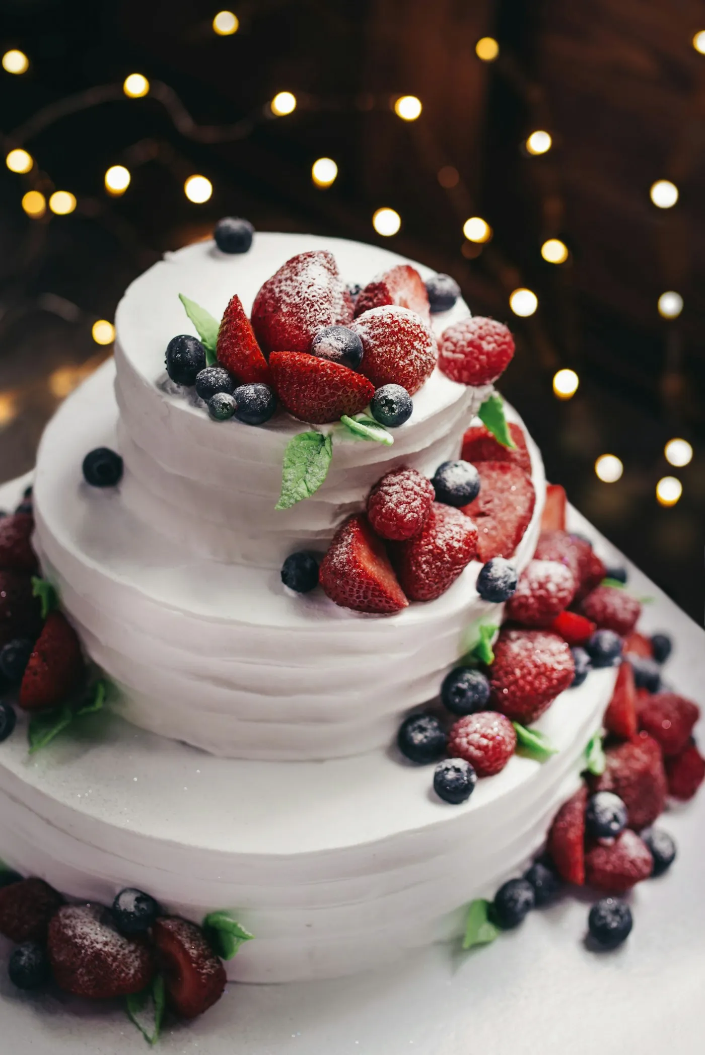 Three-tier vanilla cake topped with fresh blueberries and strawberries.