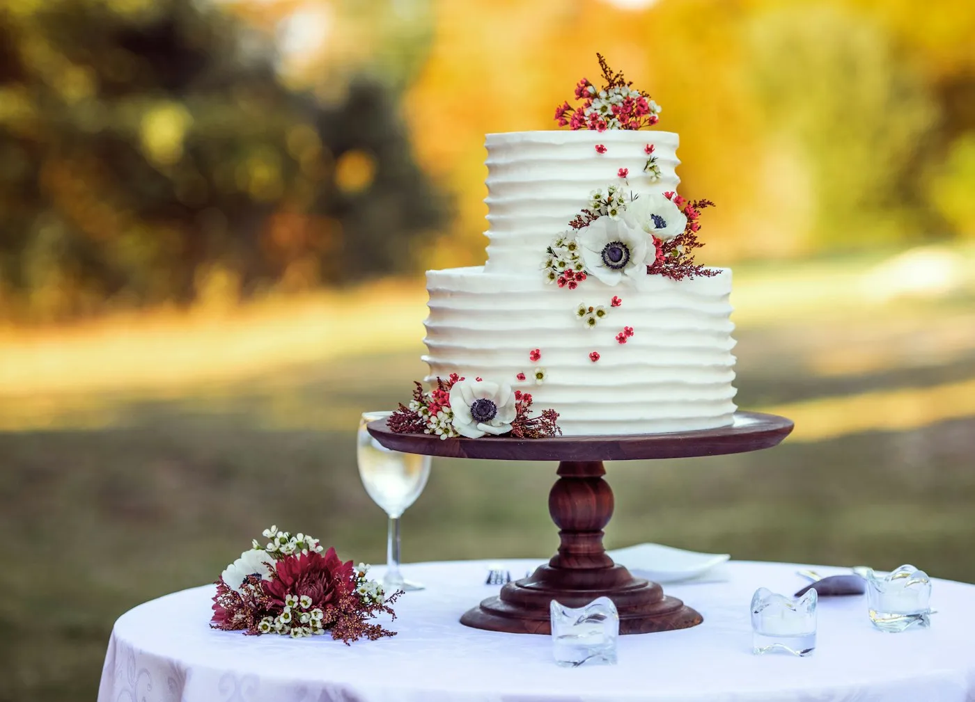 White and red floral cake on a wooden stand.